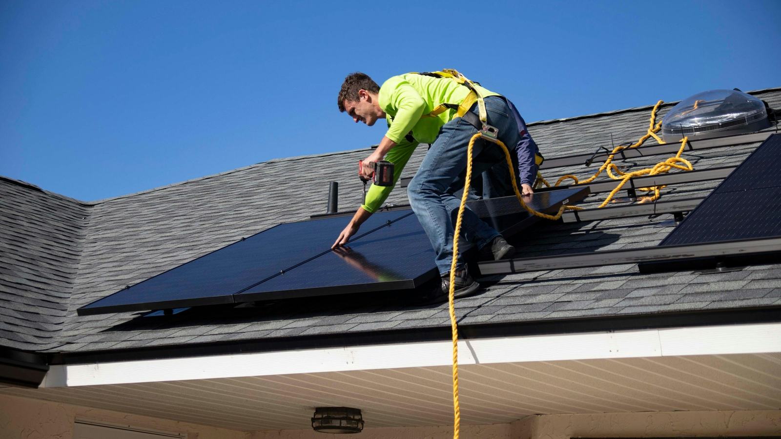 Installer securing a solar panel on a shingled roof